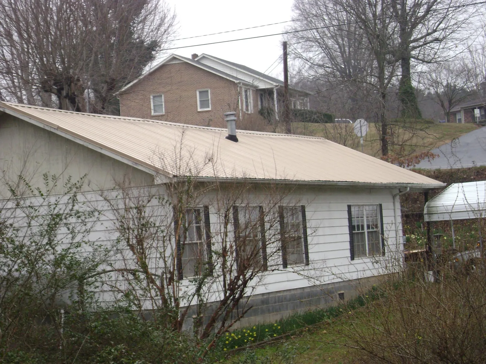 Tan metal roof on a white sided house set into a hillside — Commercial Roofing by Roofing Brothers in Newport